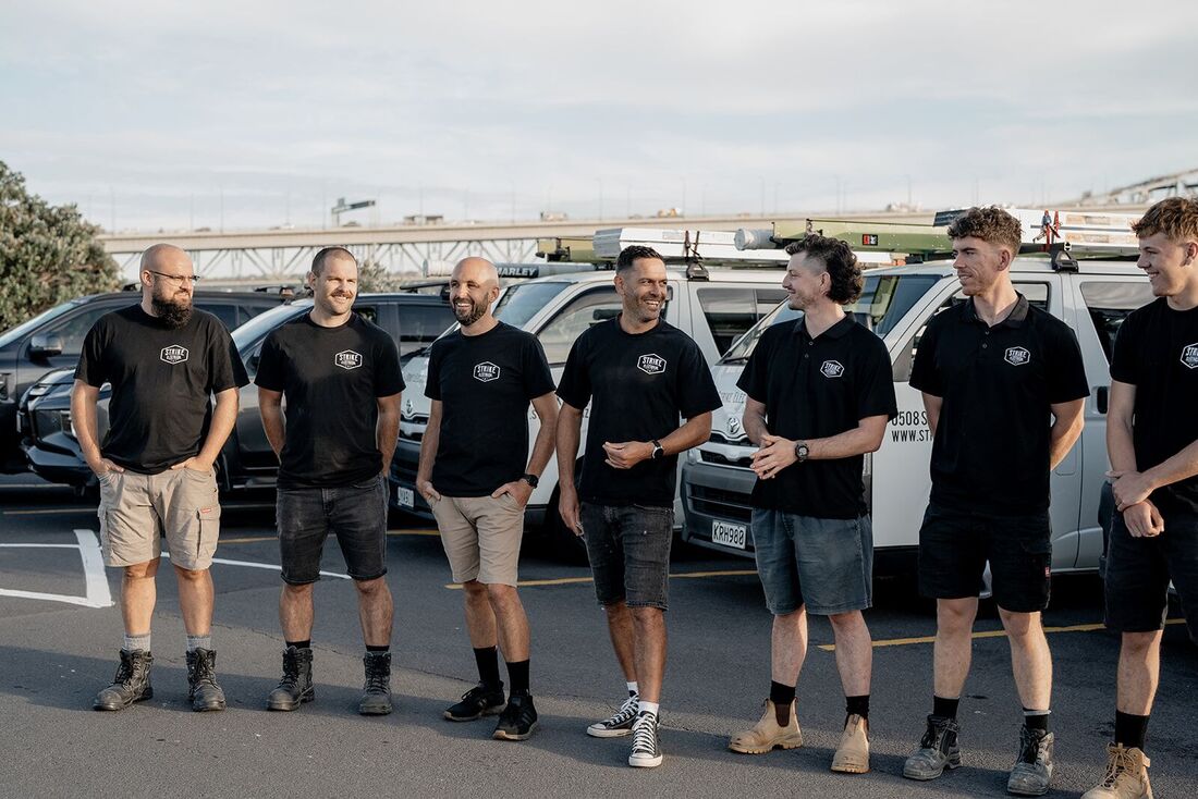 The Strike Electrical crew in branded tees in front of their fleet of vans in Auckland